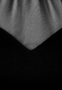 Top negro que presenta una tela negra lisa y texturizada con una superposición de color gris transparente que forma una forma de V en el escote.
