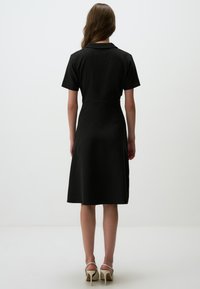 Schwarzes, geripptes Kleid mit tailliertem Schnitt, kurzen Ärmeln und einem knielangen Rock. Mit einem kragenförmigen Ausschnitt und glattem, strukturiertem Stoff.