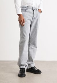 Lys grå denimjeans med rett ben-design, subtil tekstur og knappestang-lukking, kombinert med svarte slip-on sko.