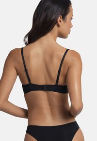 Soutien-gorge noir avec de fines bretelles réglables, une texture lisse et un système d'attache à crochets au dos. Design simple sans motifs visibles.