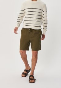 Zelené bavlněné šortky s elastickým stahovacím pasem; bílý svetr s černými vodorovnými pruhy; hnědé sandály s přezkami.