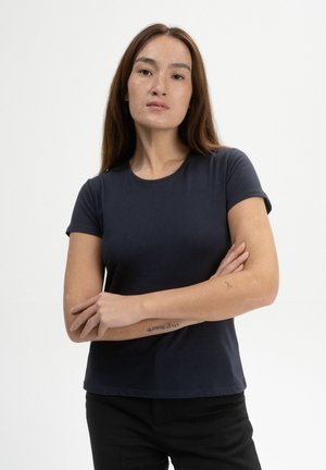 Navyblaues T-Shirt mit kurzen Ärmeln aus weichem Material, mit rundem Ausschnitt und tailliertem Schnitt, präsentiert an einem Modell mit verschränkten Armen.