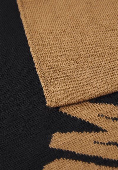 Strikket tekstil med en beige og svart fargeskala. Den beige delen har en fin, strukturert overflate, mens det svarte området har et dristig mønster.