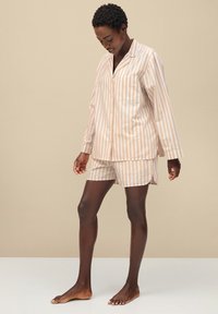 Gestreept slaapset in een zachte stof; lichtbeige met witte strepen. Het bovenstuk heeft een kraag en knopen, vergezeld van bijpassende shorts.