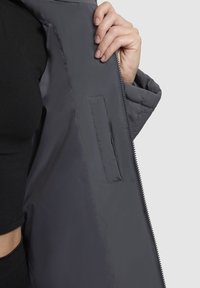 Gray insulated jacket opened to reveal a smooth interior. Features a side pocket and a contrasting zipper. Soft, lightweight material.
