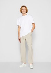 Weißes Baumwoll-T-Shirt, beigefarbene weite Hosen und weiße Slipper. Minimalistisches Design mit lockerer Passform.