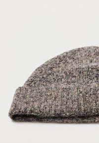 Brun og grå strikket ull-lue med brett, liggende flatt på en hvit overflate.