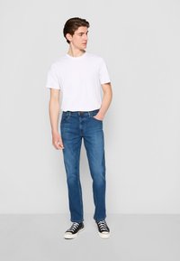 Vaqueros de mezclilla azul con corte recto, combinados con una camiseta blanca de manga corta y zapatillas negras de caña alta.