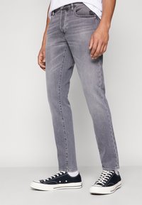 Šedé džínové kalhoty z denimu s rovnými nohavicemi, pětikapsovým designem a jemným vyblednutím; kombinované s černými teniskami s bílými podrážkami.