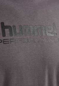 Nærbillede af gråt stof med sort og sølvfarvet tekst "hummel PERFORMANCE" trykt på.