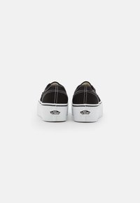 Black canvas slip-on shoes with white stitching, a raised sole, and a logo on the heel. The design features a rounded toe and elastic sides.