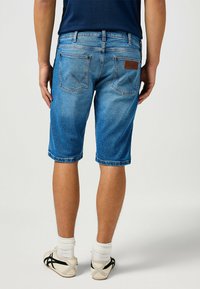 Shorts in denim di colore blu sbiadito con una vestibilità dritta, risvolti, e due tasche posteriori con un design cucito e un'etichetta in pelle.
