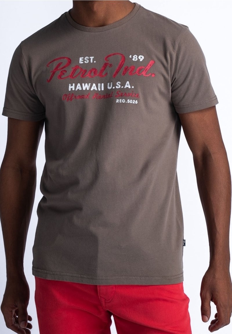 Braunes kurzärmeliges T-Shirt mit rotem und weißem Grafikspruch, auf der Vorderseite mit "Petrol Ind." und "Hawaii U.S.A." bedruckt, glatte Stofftextur.