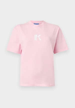 Gaiši rozā īsroku T krekls ar baltu stilizētu "K" logotipu krūtīs centrā, attēlots uz vienmuļa balta fona.