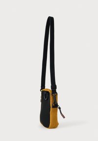 Kompaktowa torebka na ramię z czarno-żółtym połączeniem materiałów, teksturowaną powierzchnią, regulowanym paskiem oraz kieszenią na zamek z metalowymi detalami.