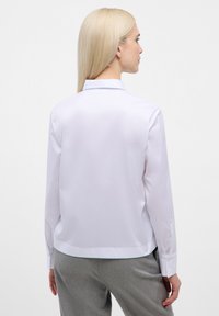 White, long-sleeve button-up shirt with a smooth texture, rounded hem, and classic collar. Features cuff buttons and a tailored fit.