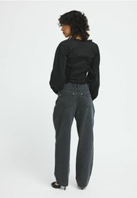 Maglietta nera a maniche lunghe con scollo arricciato e schiena aderente, abbinata a jeans neri svasati a vita alta in un lavaggio sbiadito.