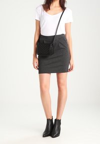Conjunto en negro y gris que incluye una falda gris ajustada, una camiseta blanca de cuello en V y botas negras hasta el tobillo. Bolso bandolera negro con patrón de chevron.
