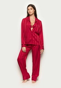 Roter Satin-Pyjama-Set mit einer Knopfleiste, vertikalen Streifen und passenden, locker sitzenden Hosen, die eine glänzende Textur aufweisen.
