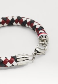 Pulsera de cuero trenzado en rojo, negro y blanco, con un cierre y acentos de metal plateado. Presenta un diseño texturizado y un cierre moderno.