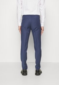 Navy tailored trousers with a smooth, textured fabric, featuring a slim fit, two back pockets, and a crease down the leg. Black footwear.