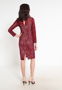 Burgunderfärgad spetsklänning med långa ärmar, dragkedja i ryggen, slits baktill och genomskinlig överdel, med ett blommönster hela vägen.