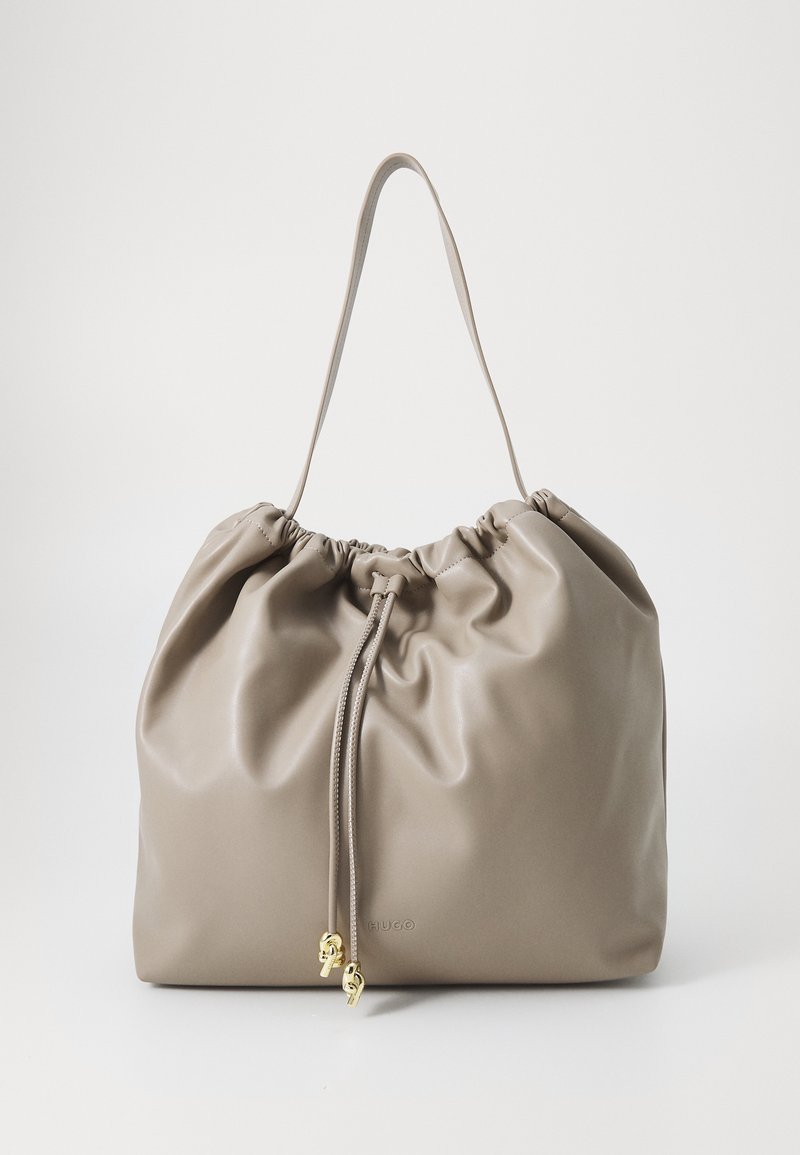 Sac à bandoulière en cuir taupe doux avec fermeture à cordon et accents de charme dorés, design minimaliste sur fond blanc.