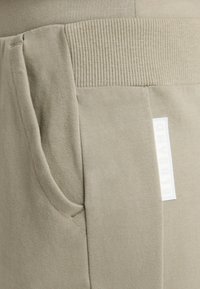 Helle graue Jogginghosen mit geripptem Bund, Seitentasche, weichem Material und einem kleinen Logolabel auf der Vorderseite eingestickt.