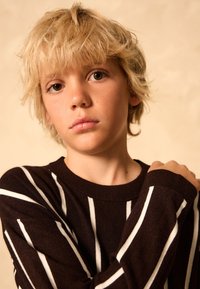 Mörkbrun tröja med vita vertikala ränder, ribbad halsringning och muddar. Mjuk textur, med avslappnad passform och lager-på-lager-stil.