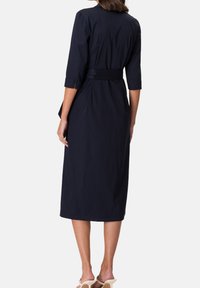 Vestido de un oscuro tono azul marino, confeccionado con una tela ligera, de longitud hasta la rodilla, con mangas de tres cuartos, cintura ceñida y un diseño sencillo y limpio.