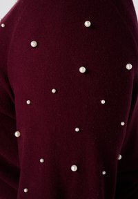 Bordeaux stof versierd met verspreide kleine en middelgrote witte parelversieringen.