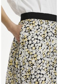 De bloemenrok heeft een zwarte achtergrond met witte en gele madeliefjes, een elastische zwarte tailleband en zijzakken.