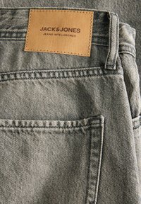 Sive traperice z usnom etiketom oznakom "JACK & JONES JEANS INTELLIGENCE" na struku, s ušivenim naglascima i minimalnim detaljima džepova.