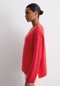 Pink knitted sweater with a V-neck, long sleeves, and side slits. Made from a textured yarn, featuring a loose, relaxed fit.