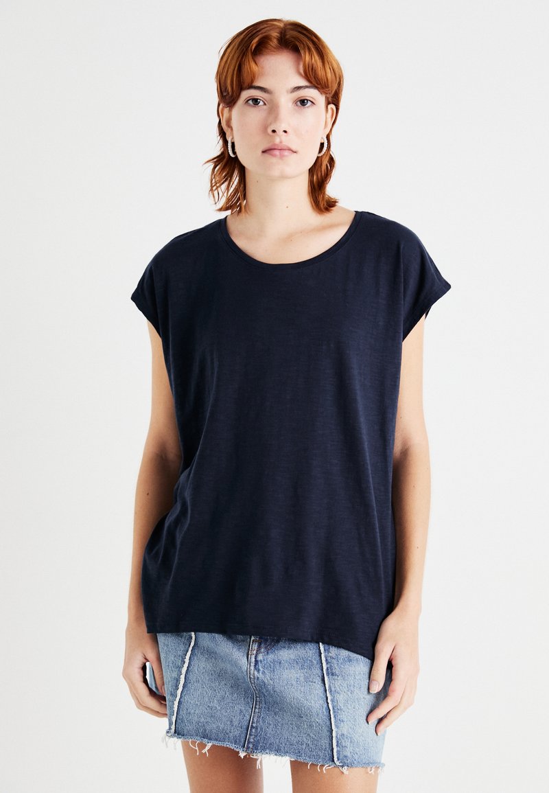 Marineblå t-skjorte med kort erm, løs passform og rund hals, kombinert med en lys denim skjørt med slitte detaljer i kanten.