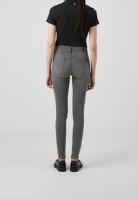 Vaqueros gris ajustados con una cintura de media altura, dos bolsillos traseros y detalle de botón, combinados con una camiseta negra de manga corta y zapatos negros.