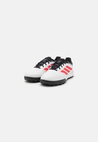 Zapatillas deportivas blancas con cordones negros y suela de goma negra. Tres franjas rojas en los lados, puntera redondeada y diseño de superficie texturizada.