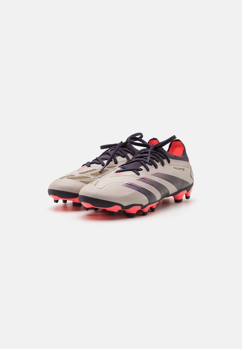 Crampons de football gris clair avec des accents violets et des semelles noires. Présente un design texturé, des lacets standards et une doublure intérieure rouge vif.