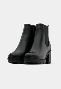 Svarta ankelstövlar med slät läderfinish, elastiska sidopaneler, chunky klack och en strukturerad gummisula för grepp.