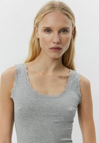 Sivi majica bez rukava s rebrastom teksturom, s čipkastim obrubom na izrezu i otvorima za ruke. Prilagođen dizajn koji se može nositi u svakodnevnim prilikama.