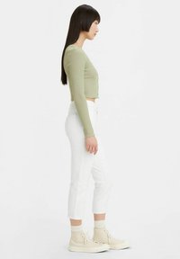 Lichtgroene ribbelachtige langarm crop top, witte recht gesneden jeans en beige hoge sneakers. Soepele textuur, aansluitend ontwerp, knoopdetails.
