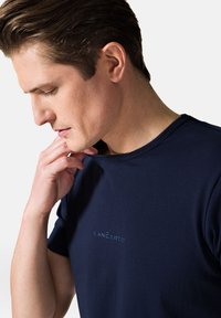 Granatowa koszulka z krótkim rękawem, wykonana z miękkiego materiału, z subtelnym logo w jaśniejszym odcieniu niebieskiego na piersi i okrągłym dekoltem.