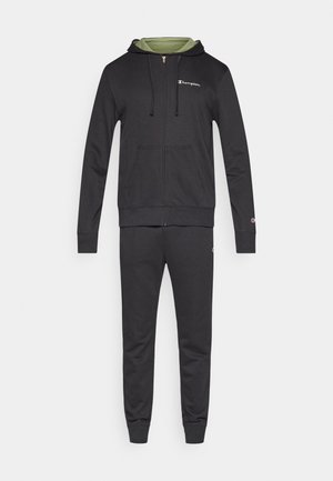 Zwarte hoodie met ritssluiting, groen binnenwerk en logo op de borst, gecombineerd met bijpassende zwarte joggingbroek. Soepele stof, casual design, elastische manchetten.