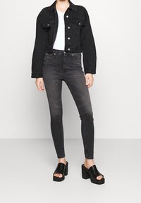 Chaqueta de mezclilla negra recortada con botones plateados, combinada con jeans skinny de tiro alto en gris oscuro y sandalias de plataforma gruesa negras.