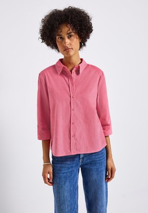 Light pink, button-up shirt with a collar and three-quarter sleeves, made of soft fabric. Paired with blue denim jeans.
