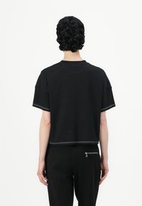 Svart kortermet t-skjorte med kontrastsøm langs kantene og rund hals. Minimalistisk design, myk tekstur.