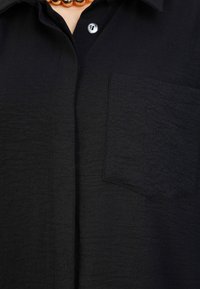 Zwarte button-up shirt van gestructureerde stof, met een borstzak en een knoopsluiting, met een kraag en zichtbare stikdetails.