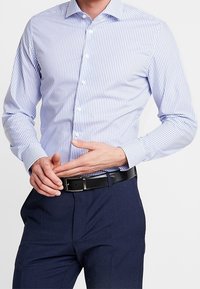 Modrá a bílá pruhovaná košile s dlouhým rukávem, s knoflíkovým zapínáním a širokým límcem, v kombinaci s tmavě modrými formálními kalhotami a černým opaskem.