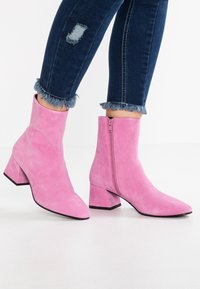 Rosa mocka ankelstövlar med spetsig tå, klack och sidodragkedja. Bärs tillsammans med jeans med fransad fåll.