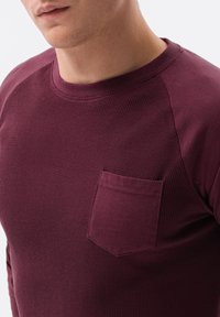Bordeaux langemouwen shirt van textuurstof, met een ronde halslijn en een klein borstzakje. Voorzien van raglanmouwen voor extra comfort.